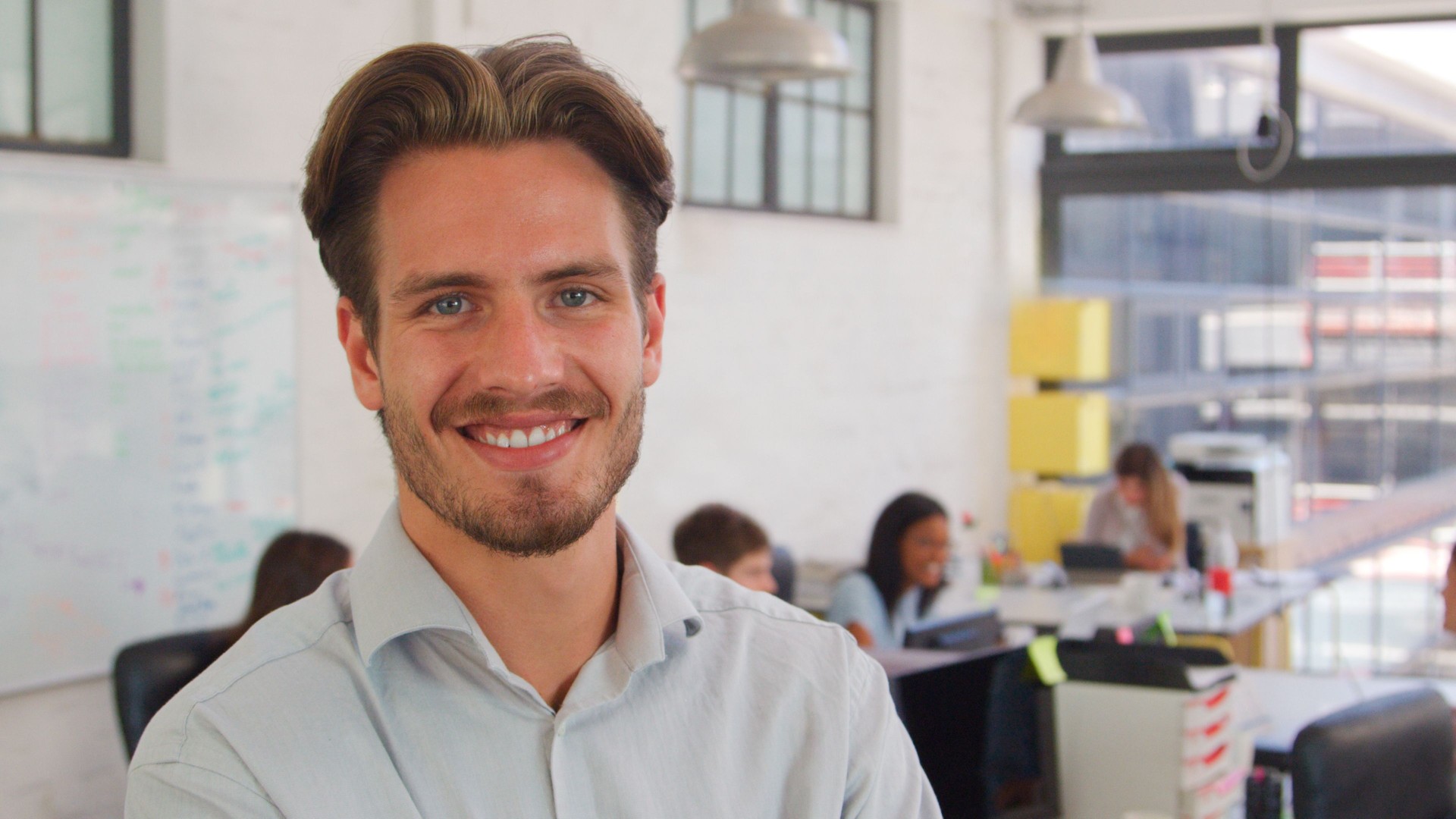 Head And Shoulders Portrait Of Smiling Young Businessman In Busy Office